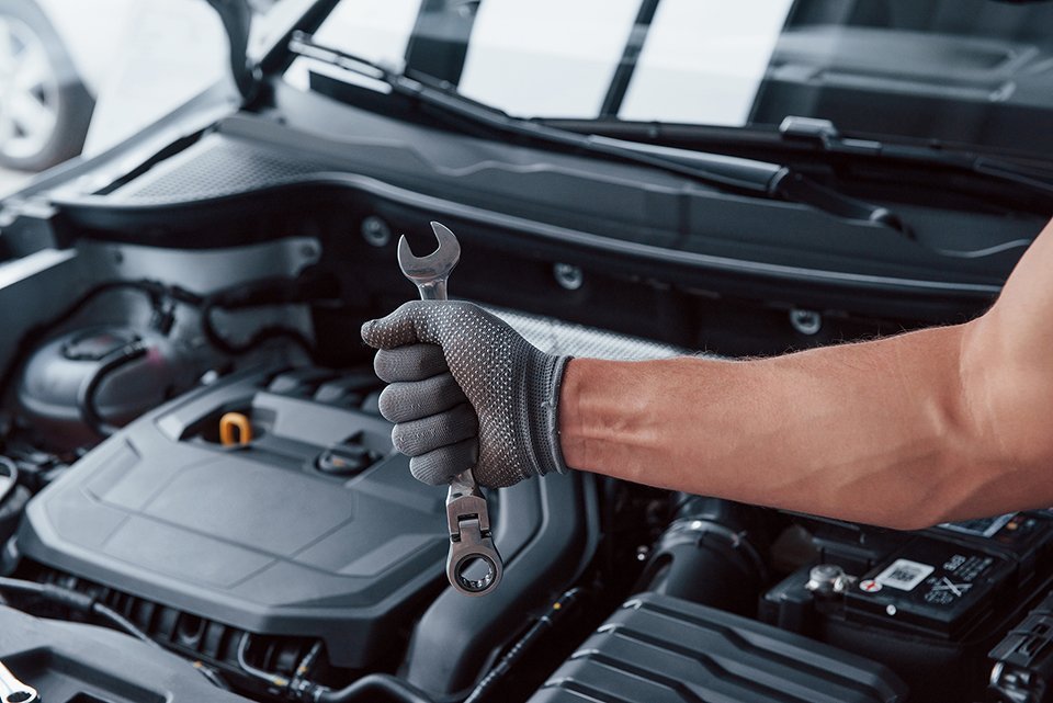 man-s-hand-in-glove-holds-wrench-in-front-of-broken-automobile.jpg